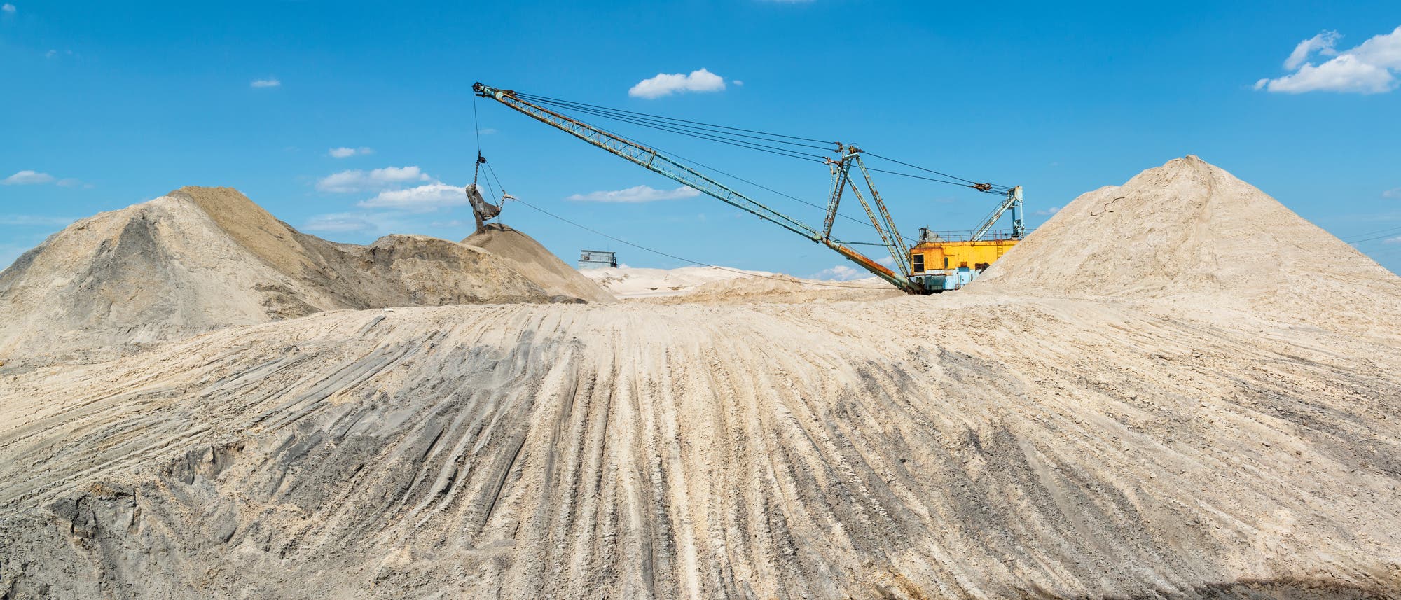 Ein großer industrielle Bagger-Maschine Sand auf einem Hügel in einem Tagebau. Im Vordergrund befindet sich rötliches Wasserteich.
