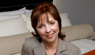 Nora Roberts posiert auf einem Bett in einem Hotelzimmer.