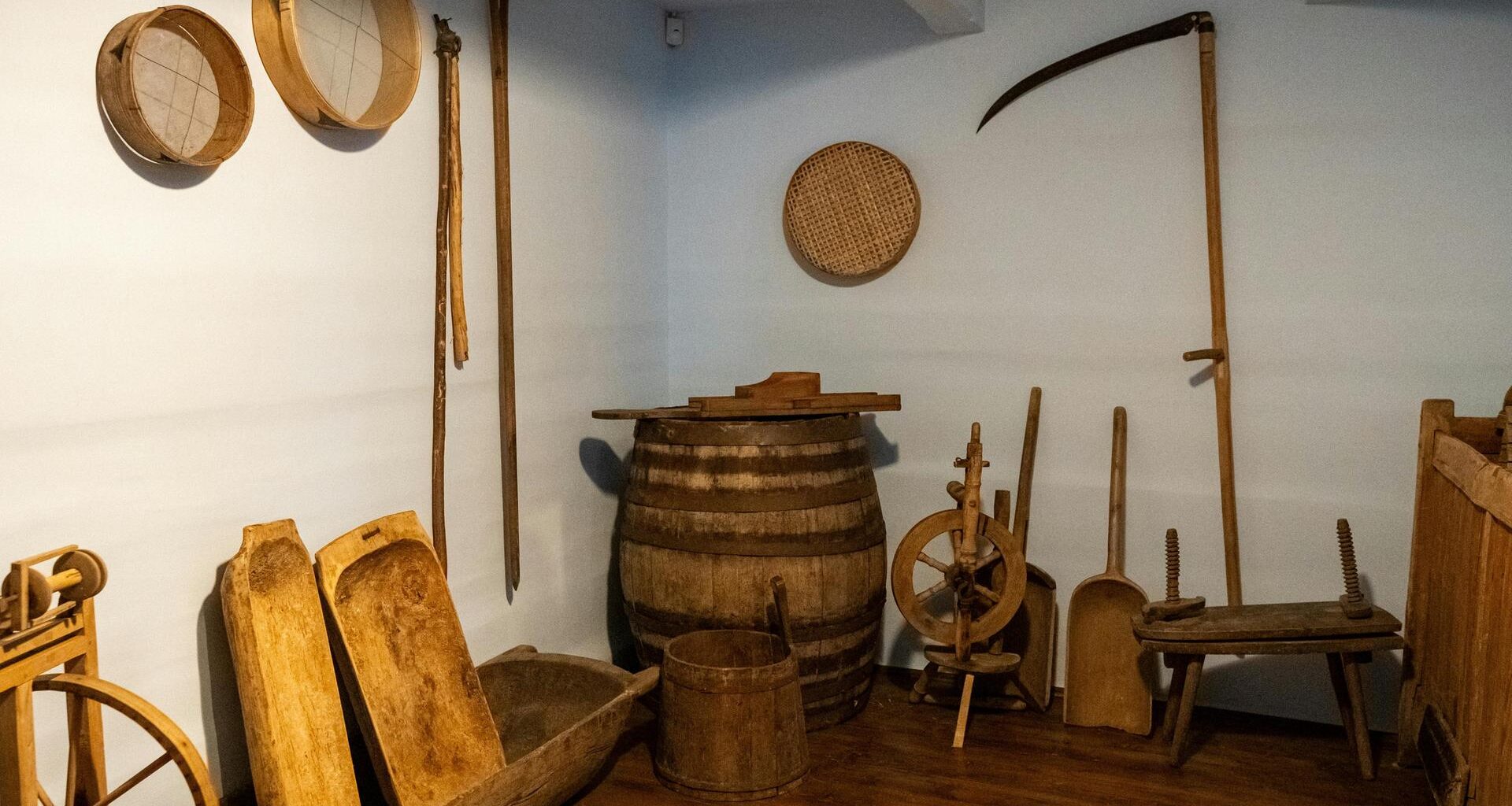 Blick in einen kellerartigen Raum in dem historische Landwirtschaftsgeräte stehen und an den Wänden hängen wie ein Spinnrad und Sensen.