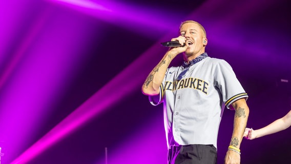 Der US-Rapper Macklemore singt in ein Mikrofon auf einer Bühne vor lilafarbenem Hintergrund. © picture alliance / ZUMAPRESS.com Foto: Daniel DeSlover