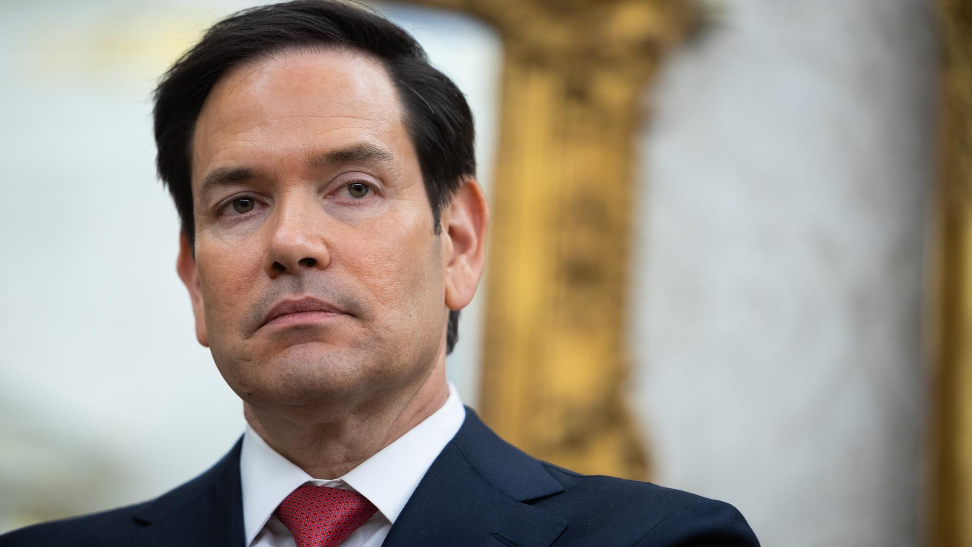 US-Außenminister Marco Rubio trägt Anzug, ein weißes Hemd und eine rote Krawatte. Sein Blick ist ernst.