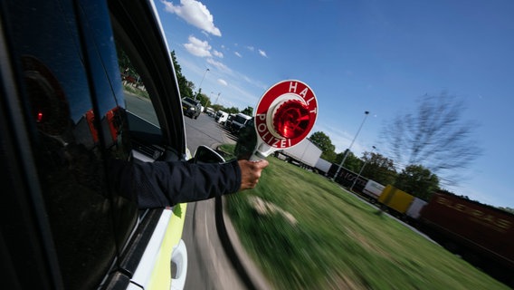 Ein Polizist streckt während der Fahrt einen Anhaltestab aus dem Einsatzwagen. © NDR Foto: Julius Matuschik