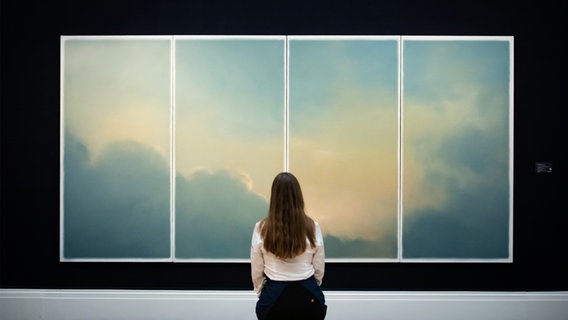 Eine Galerie-Assistentin des Auktionshauses Sotheby’s sitzt vor dem Gemälde Wolken (Fenster) von Gerhard Richter aus dem Jahr 1970. © picture alliance/dpa/PA Wire | Aaron Chown Foto: Aaron Chown