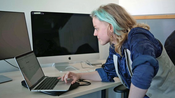 Junge Frau betrachtet einen aufgeschlagenen Laptop vor dem Hintergund vieler großer Computer © NDR.de 