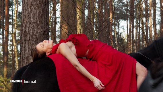 Eine Frau in einem roten Kleid liegt auf dem Rücken eines Pferdes, im Wald. © Screenshot 
