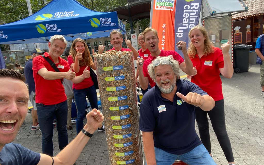 Das Team der Deutschen Postcode Lotterie vor einer Säule mit gesammelten Kippen in der Kippen-Woche.