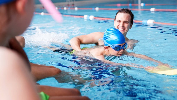 Ein Schwimmlehrer hilft einem Kind im Wasser beim Schwimmenlernen. © Imago 