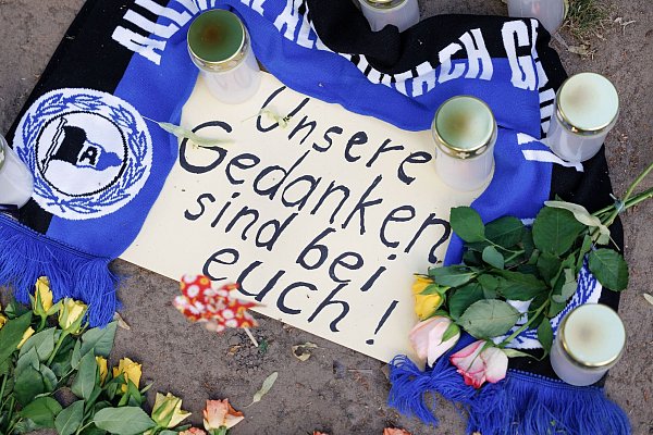 Mehrere Kerzen, ein Fanschal von Arminia Bielefeld und ein Zettel mit der Aufschrift "Unsere Gedanken sind bei Euch!" liegen kurz nach der Tat vor dem Cutie. - © Friso Gentsch/dpa