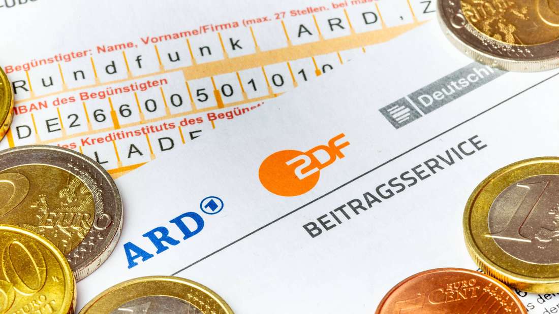 Nahaufnahme von einem Rundfunkbeitrag-Briefbogen mit ARD- und ZDF-Logo, einem Überweisungsträger und Geldmünzen
