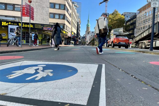 Ein Passant geht über die Kampstraße, auf der ein großes Signet „Fußgängerzone“ aufgemalt ist.