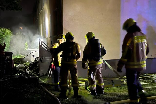 Feuerwehrleute beim Löscheinsatz an der Damaschkestraße, im Hintergrund Rauch, der aus einem Kellerfenster dringt.