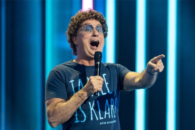 Comedian Atze Schröder steht mit einem Mikro in der Hand auf der Bühne.