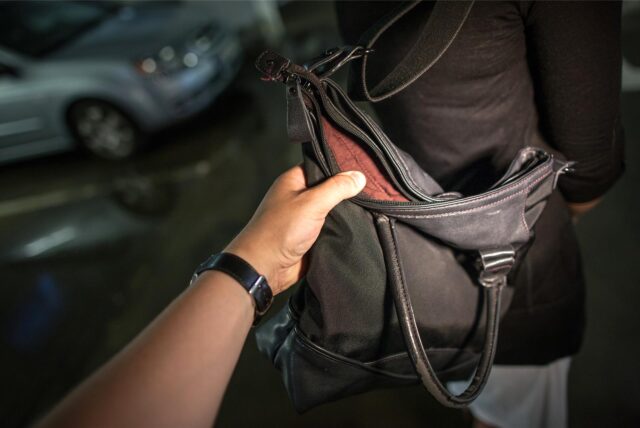 Ein Hand greift nach einer Geldbörse in einer Damenhandtasche.