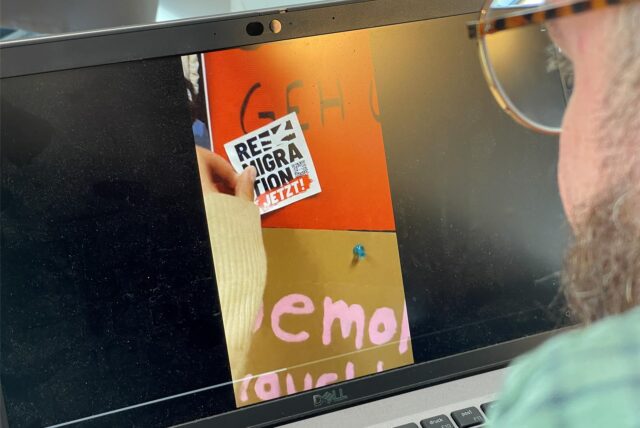 Szene aus dem Video, das Anlass für die CSG-Stellungnahme war: Die Hand der Schülerin drückt einen „Remigration jetzt!“-Sticker an die „Wand zur Demokratie“ im Schulgebäude.