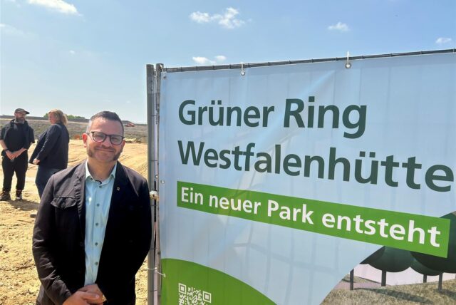 Grünflächenamts-Leiter Heike Just neben einem Transparent zum Bau des „Grünen Rings“. „Ein neuer Park entsteht“, steht darauf.