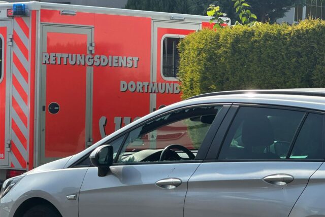 Ein Auto in Lütgendortmund mit eingeschlagener Scheibe. Im Hintergrund ist ein Rettungswagen zu sehen.