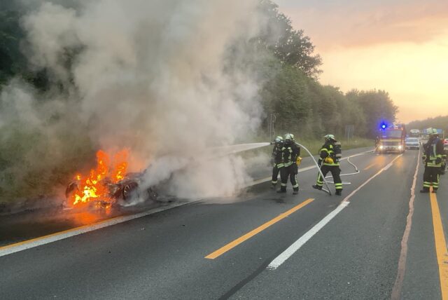 Feuerwehrleute löschen ein brennendes Auto auf einer Autobahn.