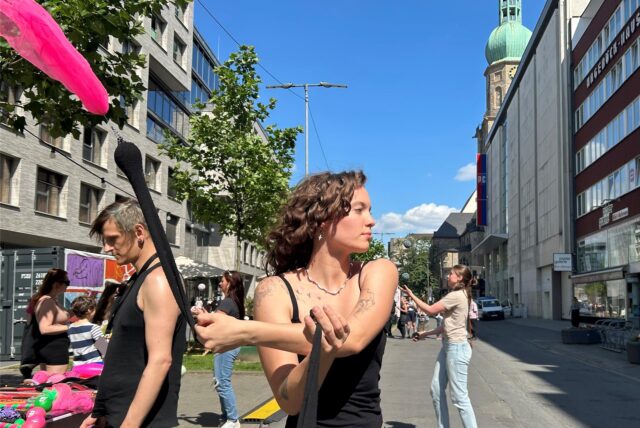 Eine junge Frau jongliert auf der Kampstraße mit bunten Bändern.