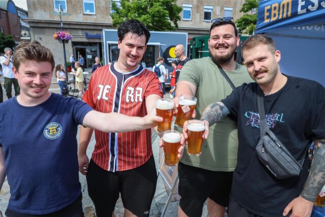 Vier Männer stehen auf dem Friedensplatz, prosten sich mit Bier zu.