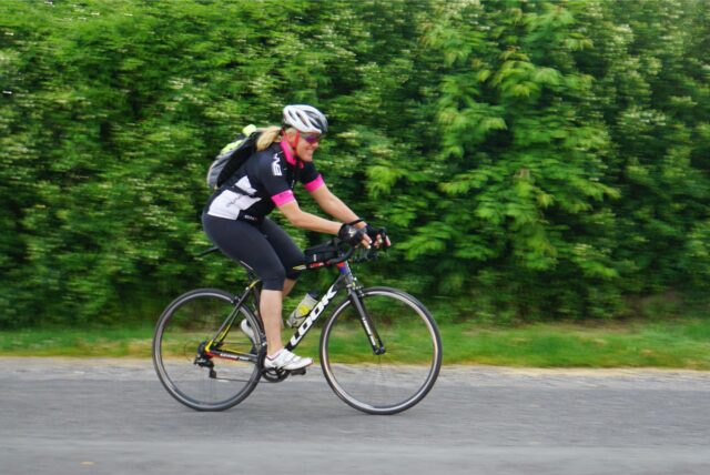 Eine Frau fährt mit einem Rennrad auf einer Straße. Sie trägt einen Helm und Radsportbekleidung.