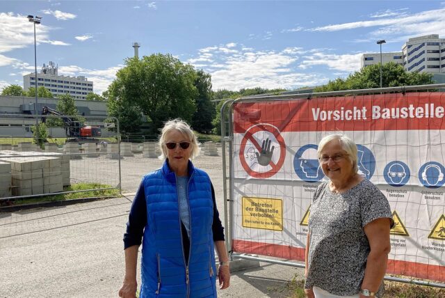 Zwei Frauen stehen vor einem Parkplatz am Berufsförderungswerk in Dortmund-Hacheney. Ein Schild im Hintergrund weist auf eine Baustelle hin.