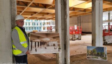 Ein Mann mit Schutzhelm hält ein Foto auf einer Baustelle