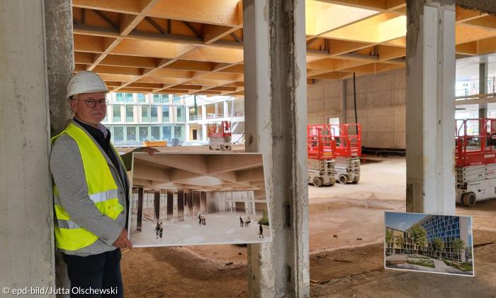 Ein Mann mit Schutzhelm hält ein Foto auf einer Baustelle