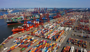 Luftaufnahme eines großen Containerhafens mit zahlreichen Containern, Kränen und Frachtschiffen.
