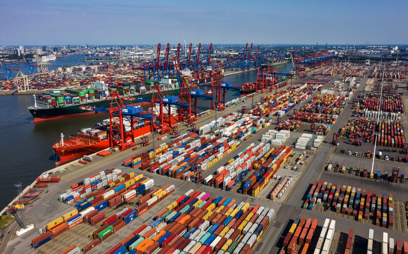 Luftaufnahme eines großen Containerhafens mit zahlreichen Containern, Kränen und Frachtschiffen.