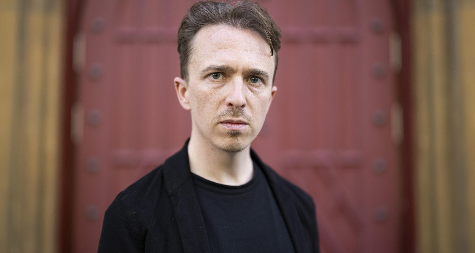 Der Schweizer Schriftsteller Béla Rothenbuehler posiert vor einem Tor.