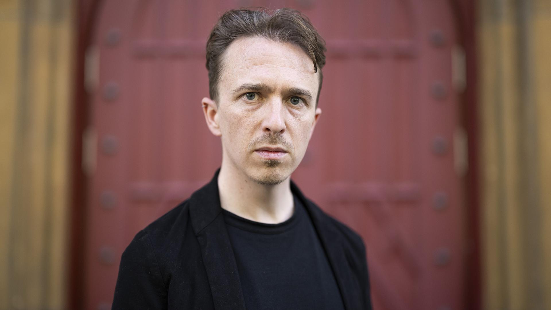 Der Schweizer Schriftsteller Béla Rothenbuehler posiert vor einem Tor.  