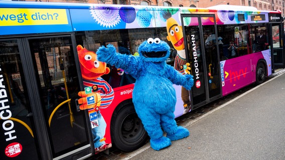 Eine als Krümelmonster verkleidete Person steht vor einem Linienbus der Hamburger Hochbahn, der anlässlich des 50-jährigen Jubiläum der Sesamstraße mit den Figuren Ernie (l.) und Bert beklebt ist. © picture alliance / dpa Foto: Daniel Bockwoldt