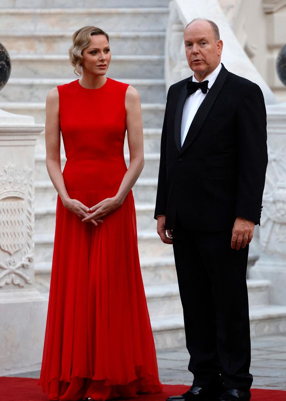 Fürstin Charlène in roter Robe neben Fürst Albert II. in Anzug