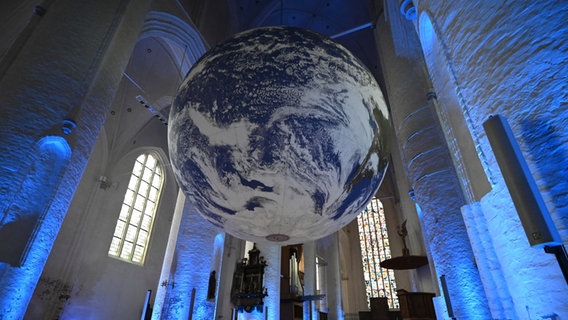 Eine riesige Weltkugel hängt unter der Decke in einer Kirche. Die Kirche ist blau beleuchtet. © picture alliance/dpa | David Hammersen Foto: David Hammersen