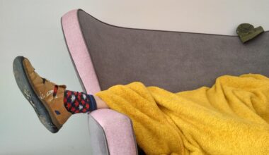 Eine Person liegt zugedeckt auf einem Sofa. Unter der Decke schaut ein Fuß heraus, der in einem Hausschuh und bunt gemusterten Socken steckt.