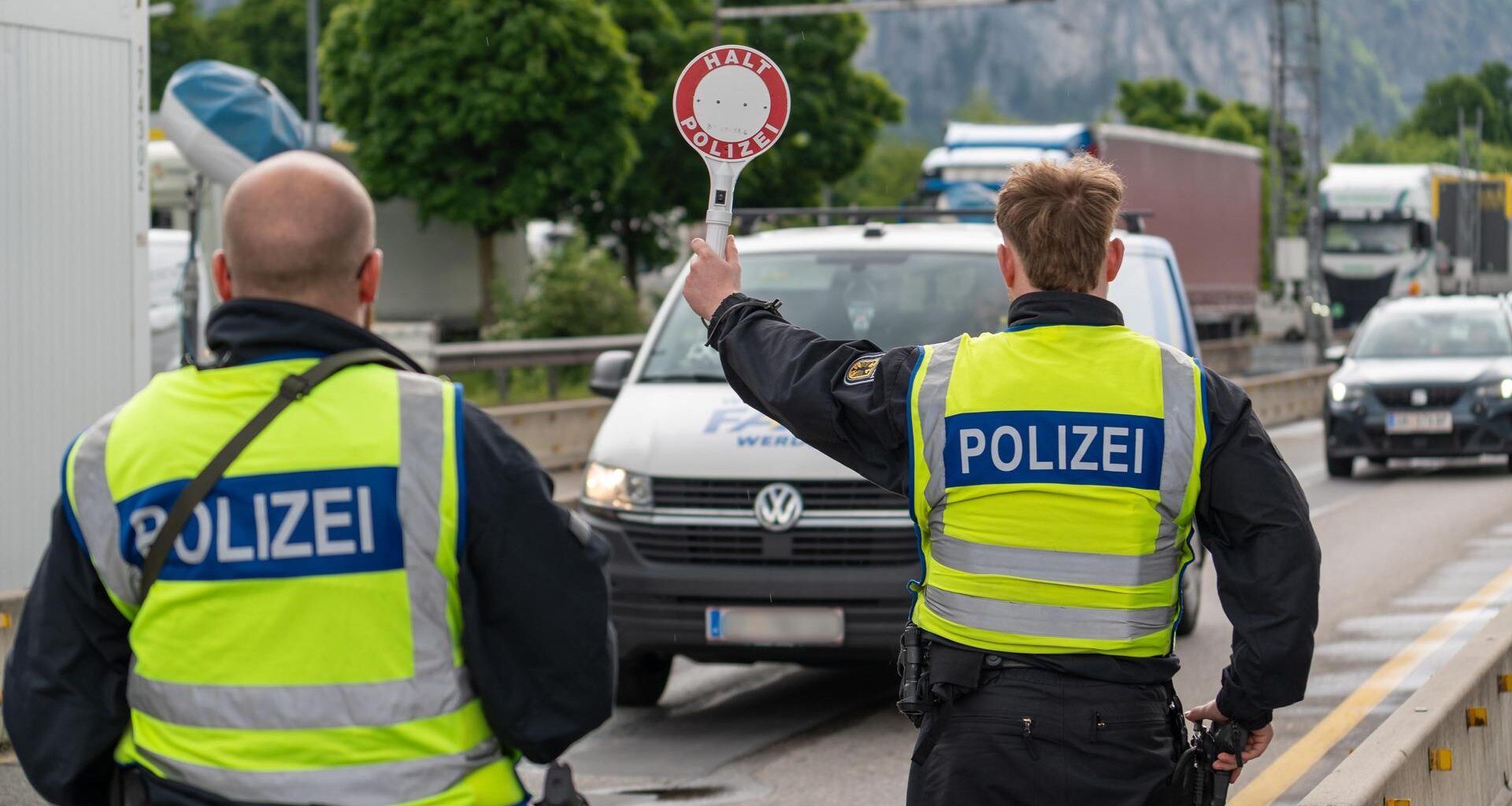 Ein Polizist stoppt an der deutsch-österreichischen Grenze ein Fahrzeug auf der Autobahn mit einer Polizeikelle mit Aufschrift: HALT POLIZEI.