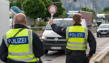 Ein Polizist stoppt an der deutsch-österreichischen Grenze ein Fahrzeug auf der Autobahn mit einer Polizeikelle mit Aufschrift: HALT POLIZEI.