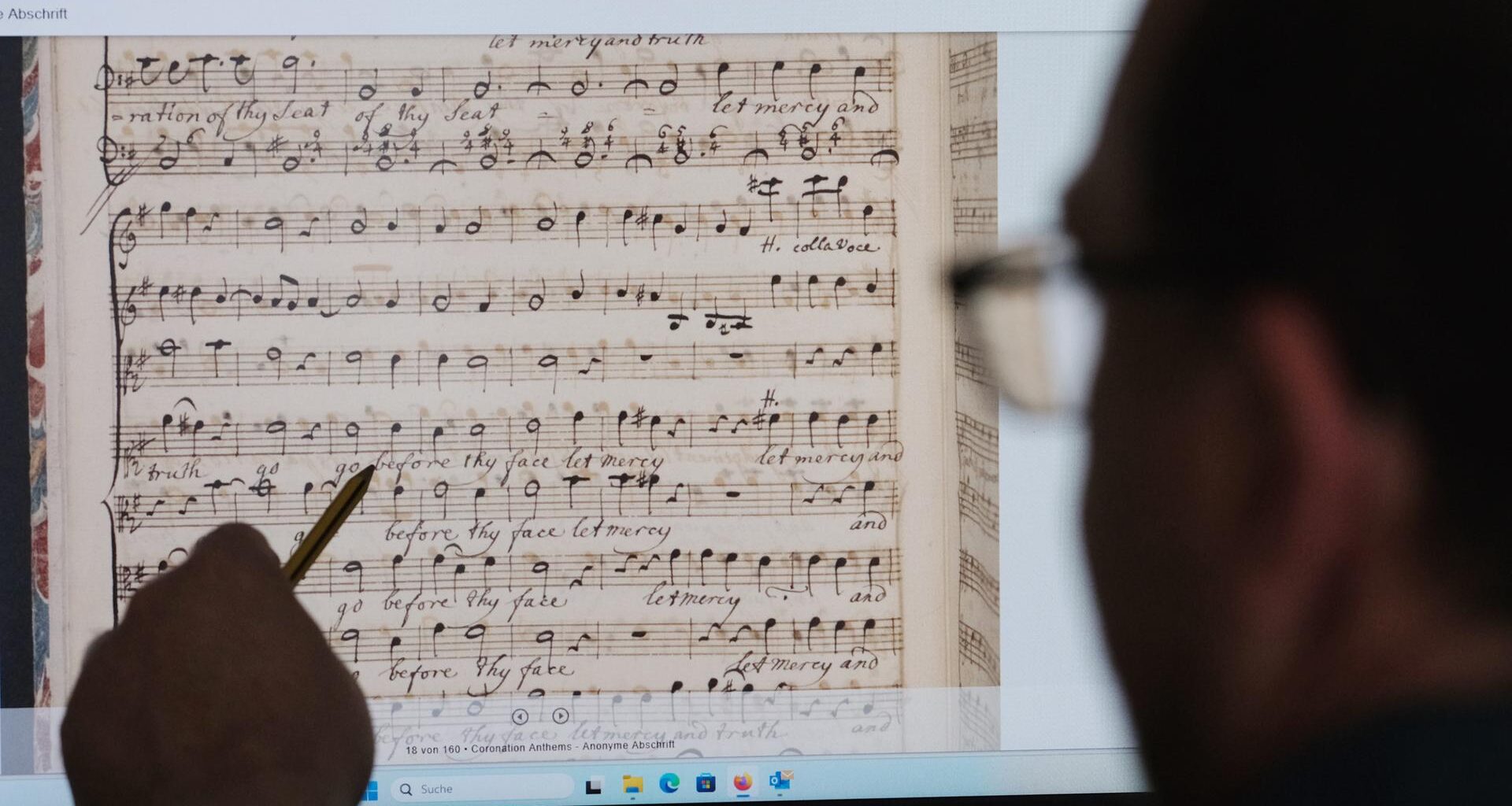 Ein Mann sitzt vor einen Computerbildschirm. Er zeigt mit einem Stift darauf. Zu sehen sind gescannte Partituren von Georg-Friedrich-Händel.