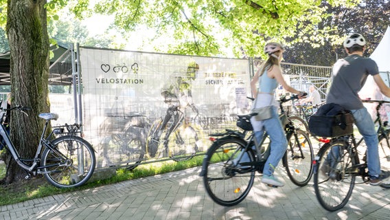 Zwei Menschen fahren Fahrrad. Im Hintergrund das Banner für die Velostation der Kieler Woche. © Landeshauptstadt Kiel Foto: Lh Kiel / Manuel Weber