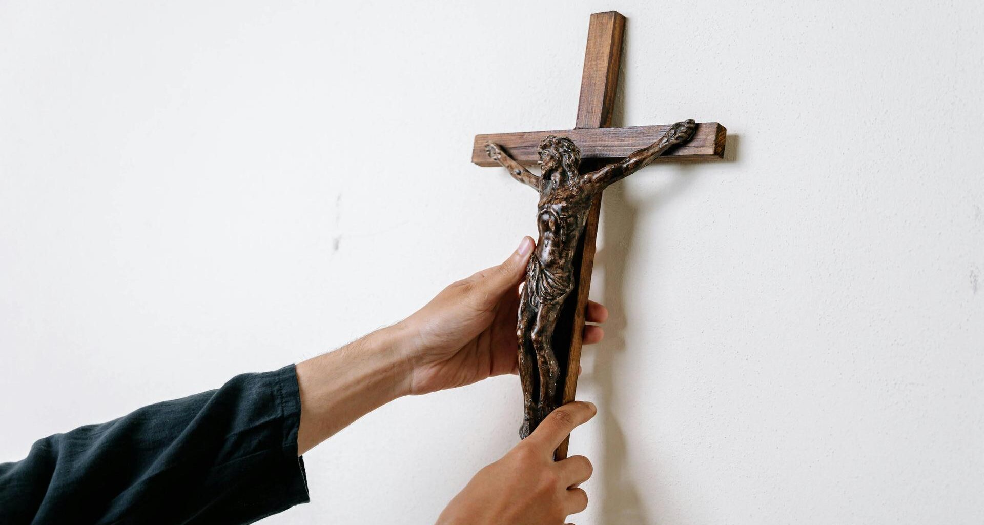 Ein Mann hängt ein Kruzifix an eine Wand.