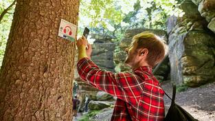 Ein junger Wanderer scannt einen QR-Code am Wanderweg mit dem Smartphone ab (Foto: Marcus Gloger | Tourismus Zentrale Saarland)