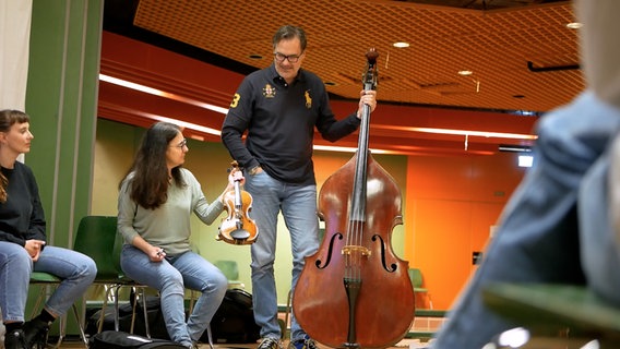 Ein Mann und eine Frau halten Geige und Kontrabass nebeneinander. © NDR RPH 