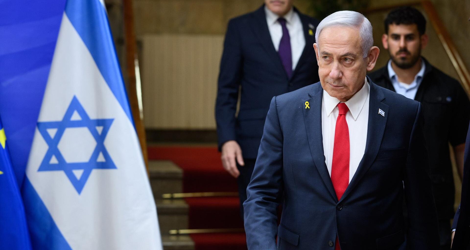 Benjamin Netanjahu, Ministerpräsident von Israel, läuft eine Treppe hinunter, ein Personenschützer ist hinter zu sehen. Neben ihm ist die Flagge Israels zu erkennen.