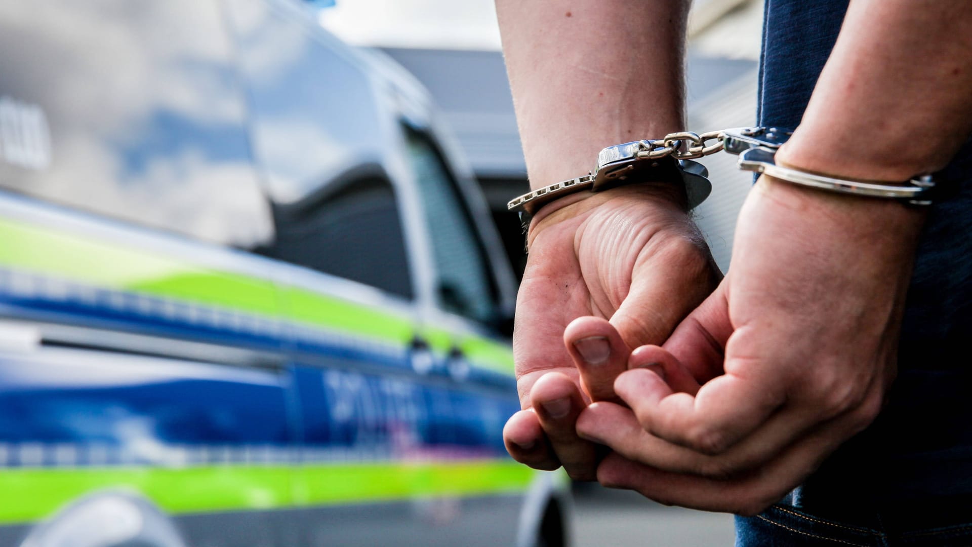 Person in Handschellen neben einem Polizeifahrzeug (Symbolbild): Der Mann soll insgesamt zwölf Diebstähle begangen haben.