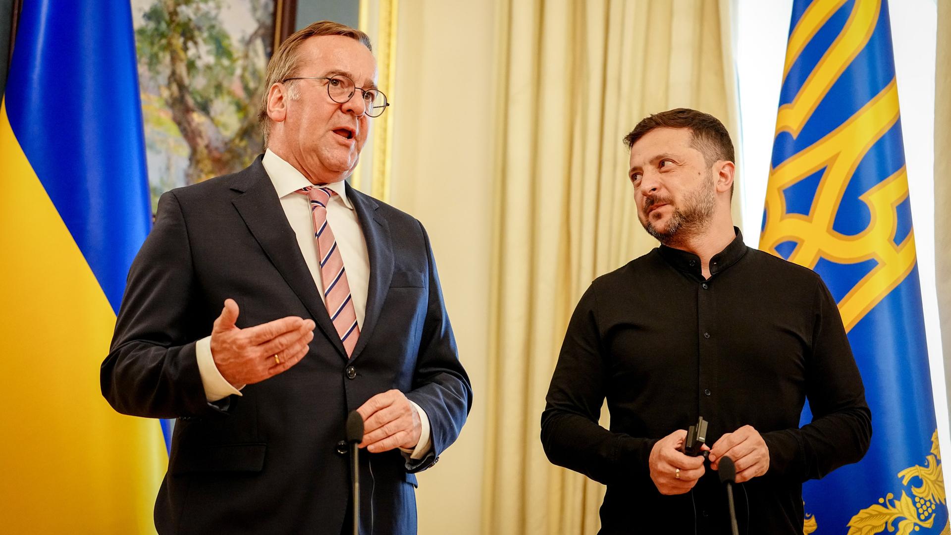 Bundesverteidigungsminister Boris Pistorius und der ukrainische Präsident Wolodymyr Selenskyj. Sie stehen nebeneinander und Pistorius spricht. Selenskyj schaut ihn von der Seite an.