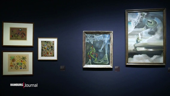 An einer Wand in einer Ausstellung hängen Gemälde im Stil des Surrealismus. © Screenshot 