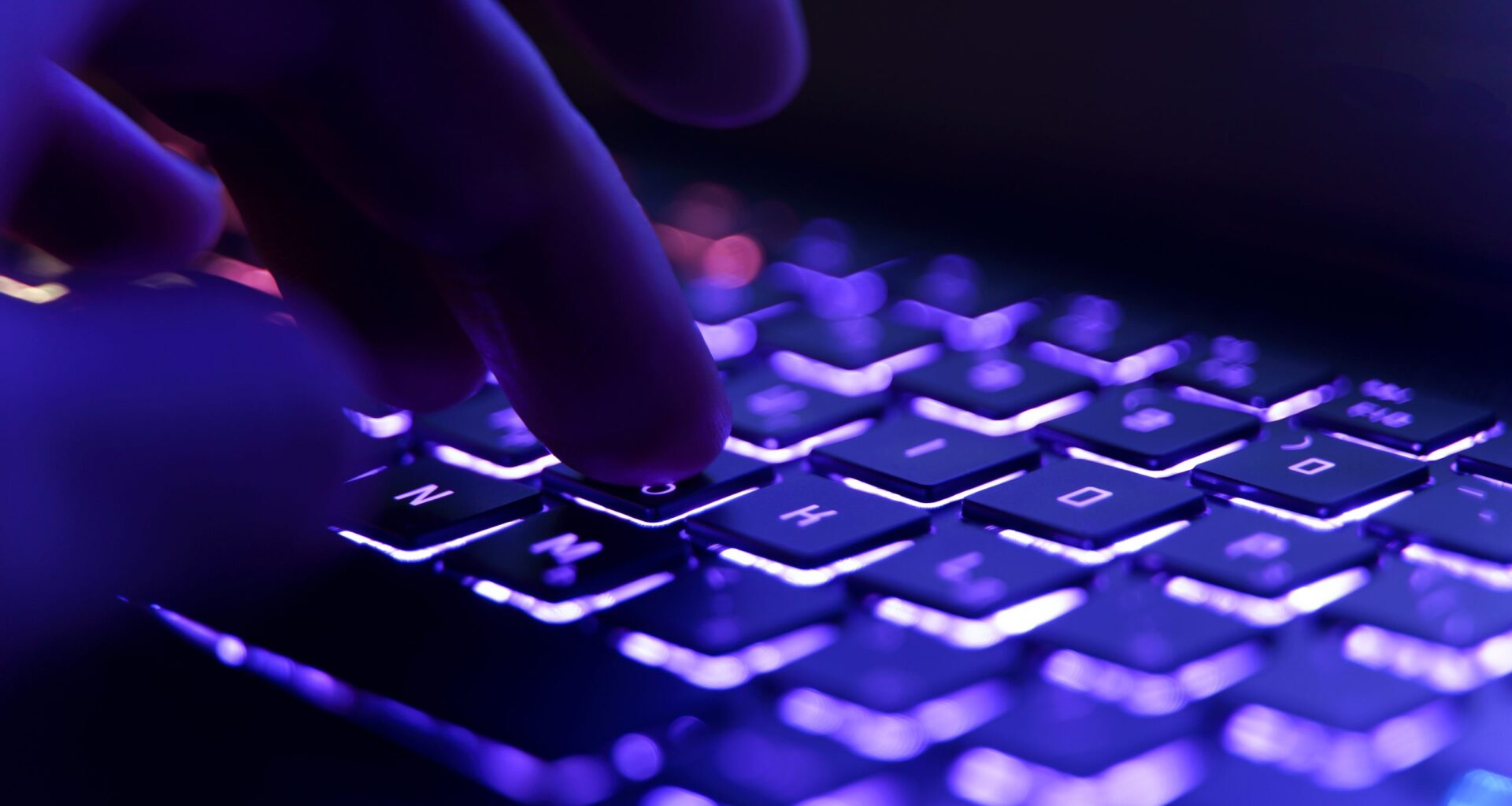 Eine Nahaufnahme der Finger einer Person, die auf einer hintergrundbeleuchteten Tastatur mit violetter und blauer Beleuchtung tippt, was auf die Gefahr hinweist, dass Anmeldedaten bei einem kürzlich erfolgten Datenleck geleakt werden.