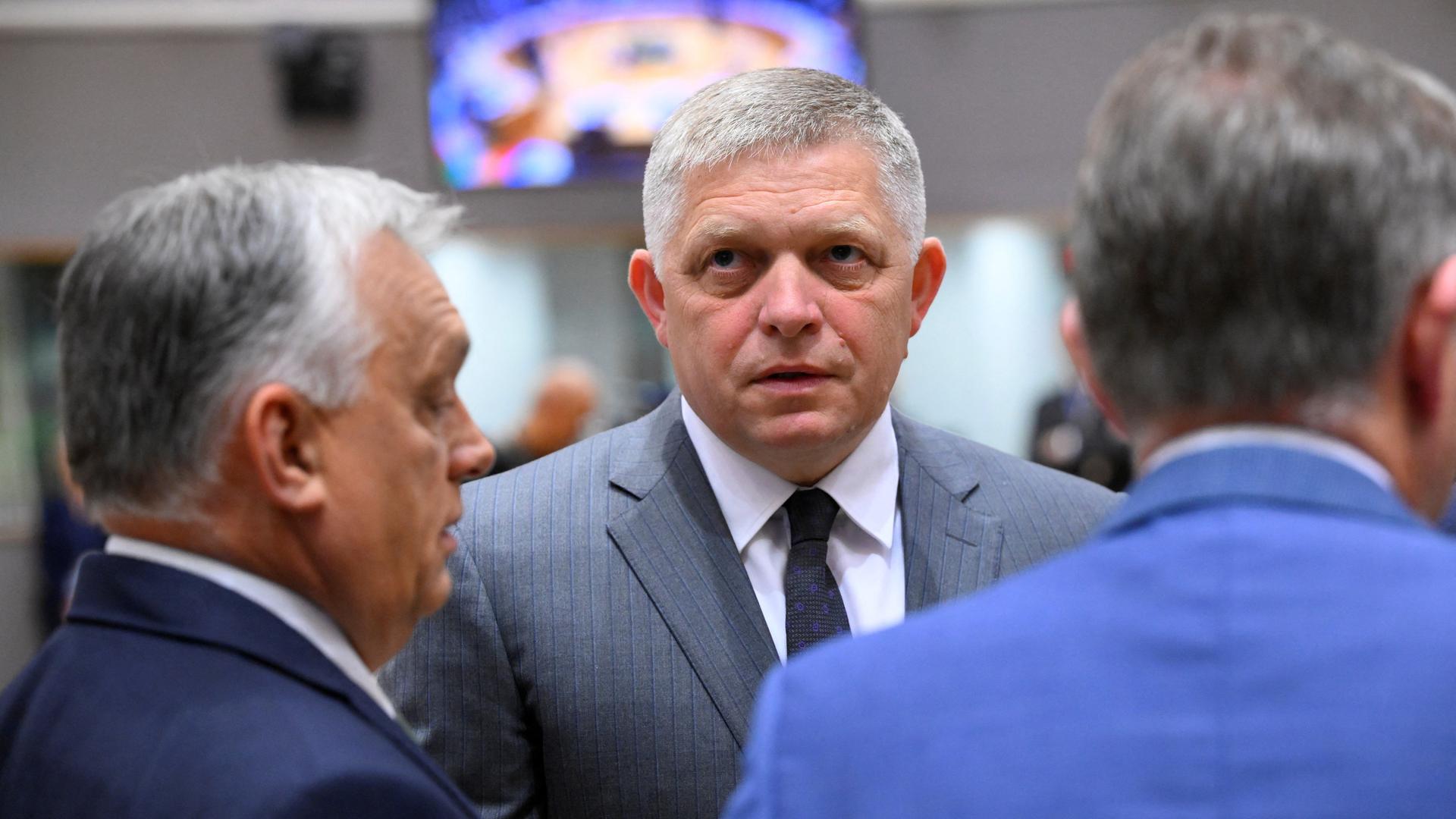 Der slowakische Premierminister Fico spricht mit dem ungarischen Ministerpräsidenten Orban, den man von der Seite sieht. Neben ihm steht ein unbekannter Mann mit dem Rücken zur Kamera.