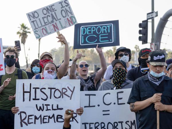 EDITORS NOTE: Graphic content / People hold placards as protesters clash with law enforcement in the streets surrounding the federal building during a protest following federal immigration operations in Los Angeles, California, on June 8, 2025. Demonstrators torched cars and scuffled with security forces in Los Angeles on June 8, as police kept protestors away from the National Guard troops President Donald Trump sent to the streets of the second biggest US city. (Photo by RINGO CHIU / AFP)