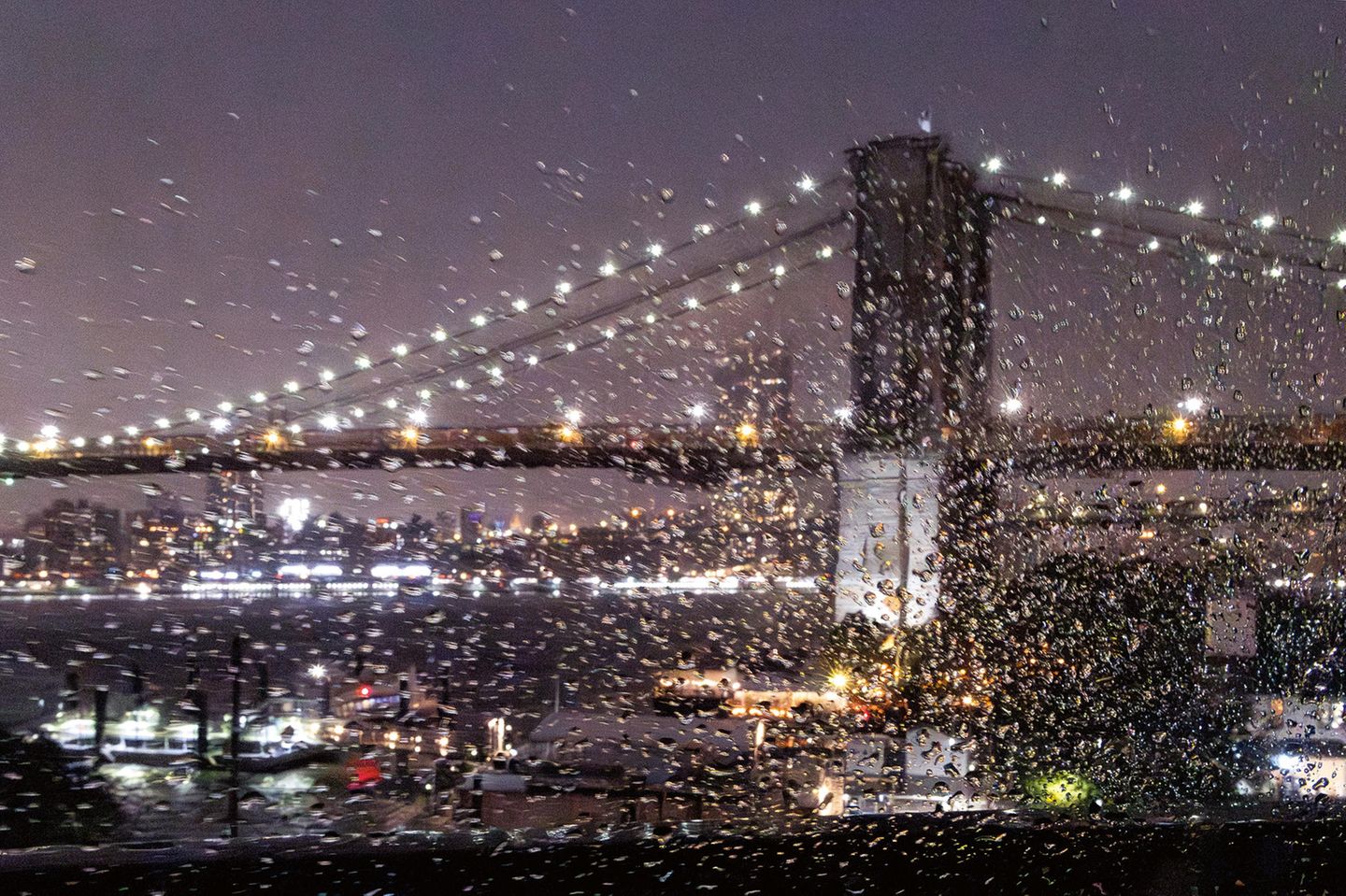 Verschwommene Aufnahme der Brooklyn Bridge bei Nacht, mit regennasser Fensterscheibe